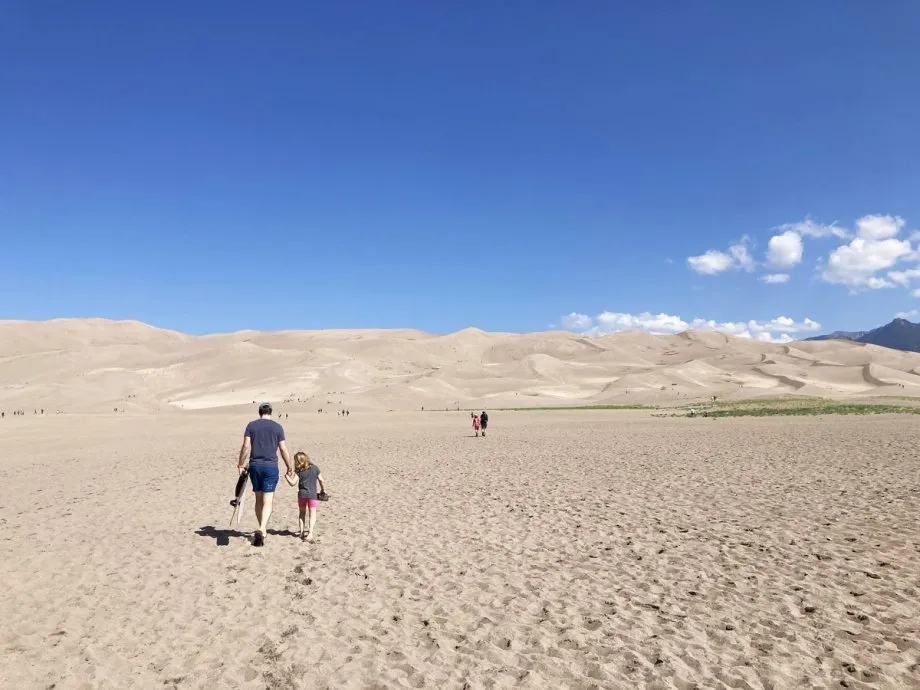 Man and Child Walking Across the Flats to the First Sand Dune for Sand Sledding