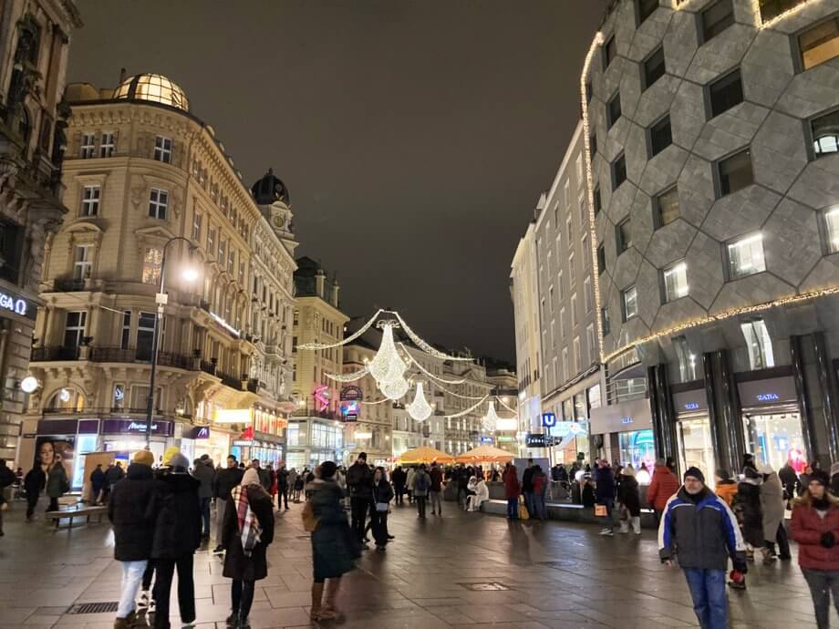 Graben pedestrian street in Vienna with lots of people and lit up by Christmas lights hanging above the street