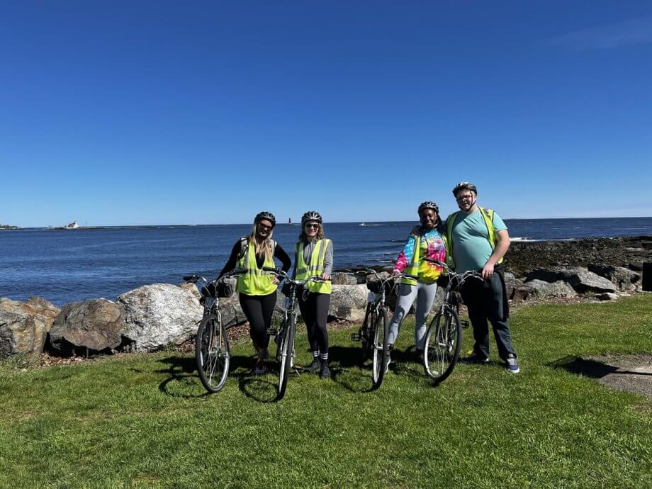 People with bikes on a bike tour with the ocean behind them, Boston to Portland road trip.