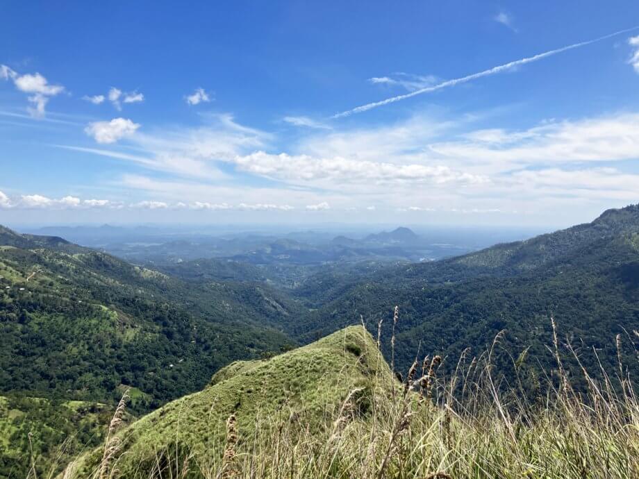 Viewpoint from Little Adams Peak, green covered mountains and blue sky looking into the distance, in Ella Sri Lanka