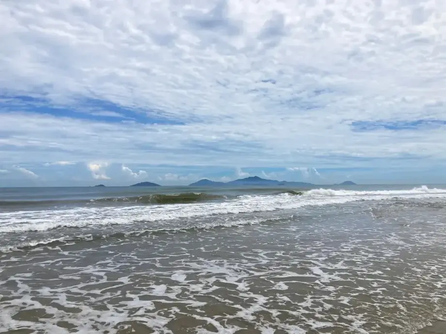 An Bang Beach with surf and sand in front and the Cham Islands behind with an even layer of clouds above.