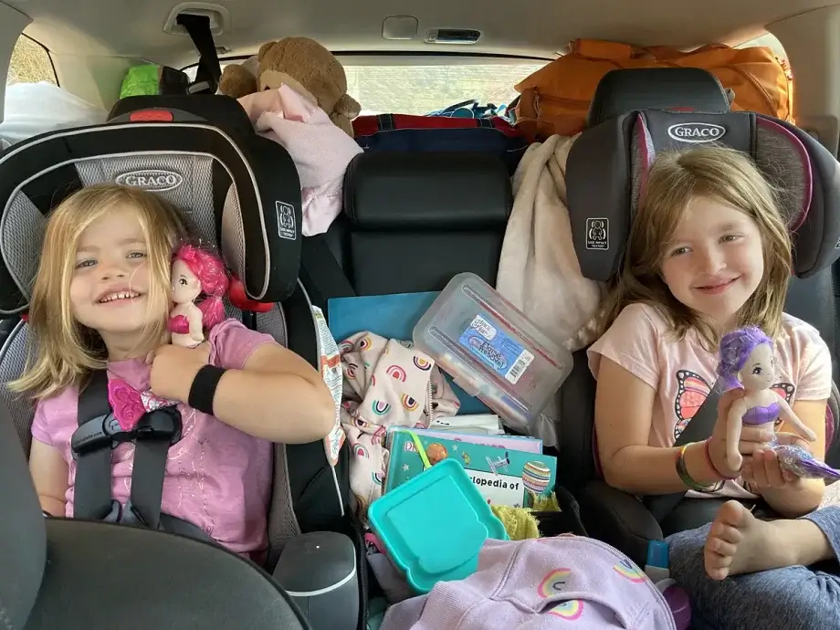 Our two girls in the backseat in their car seats with a lot of stuff around them on a family road trip